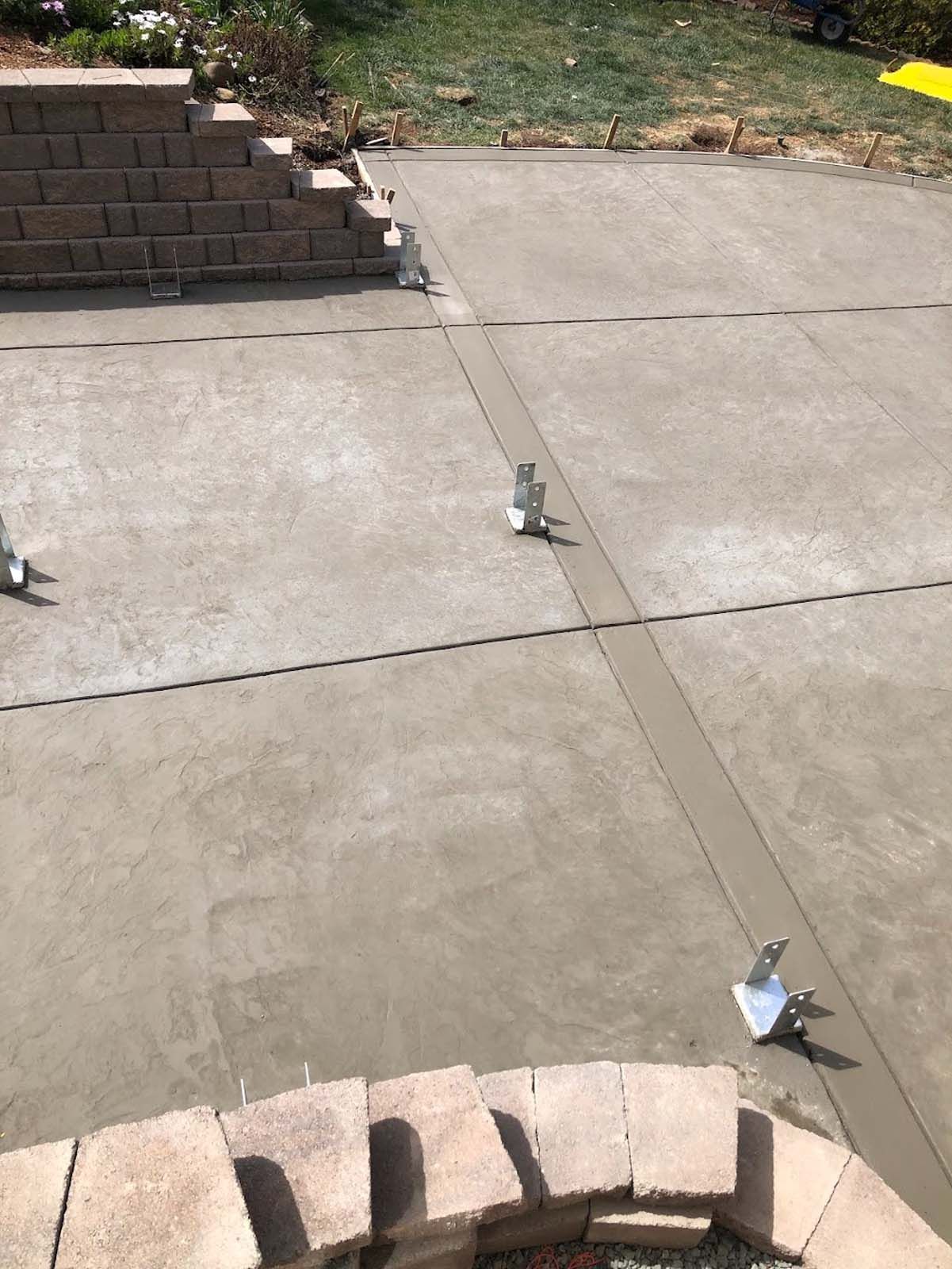 Concrete patio with expansion joints, metal anchors, and a brick retaining wall.