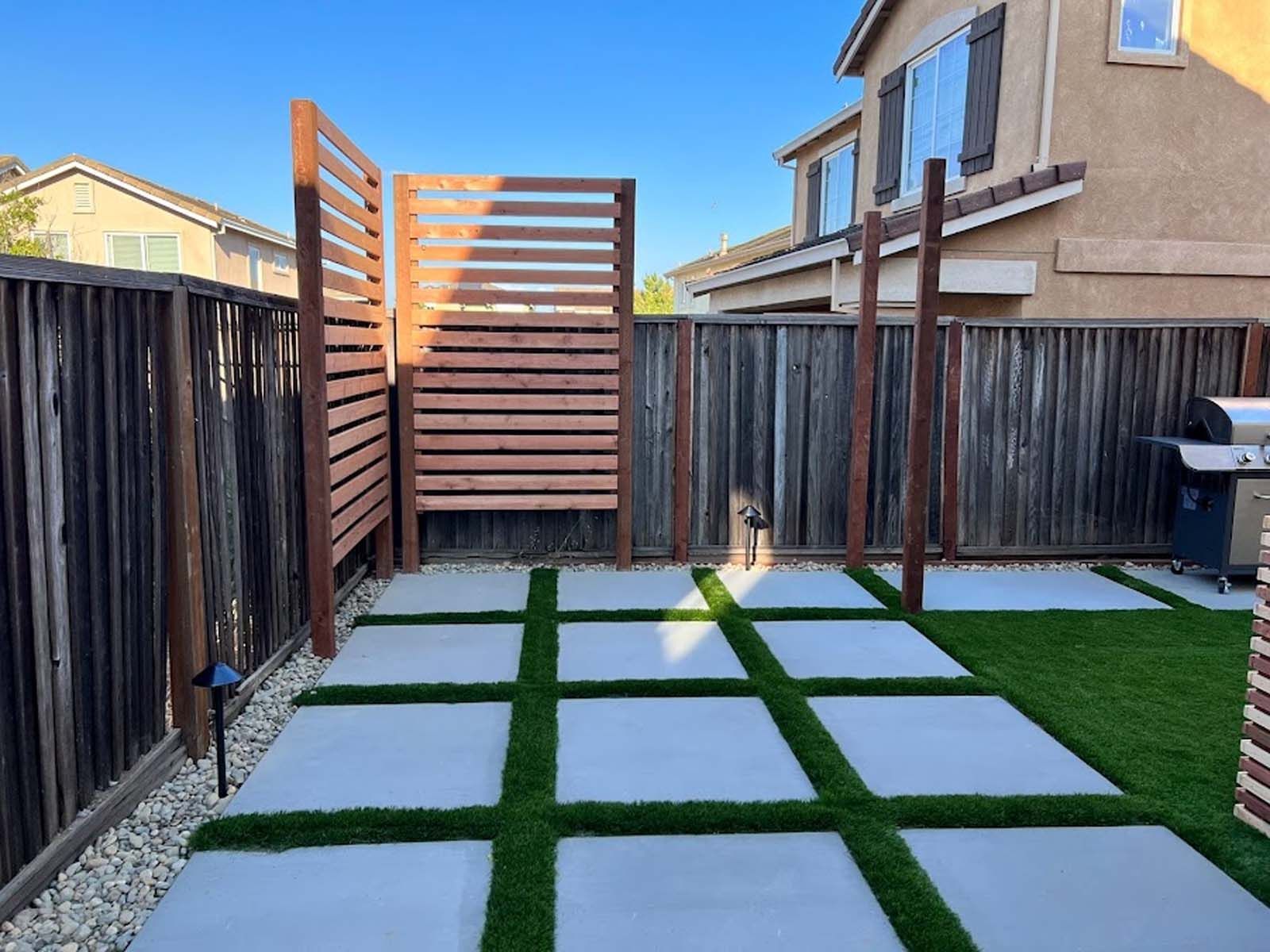 Backyard with concrete pavers, faux grass, a wooden privacy screen, and a dog.