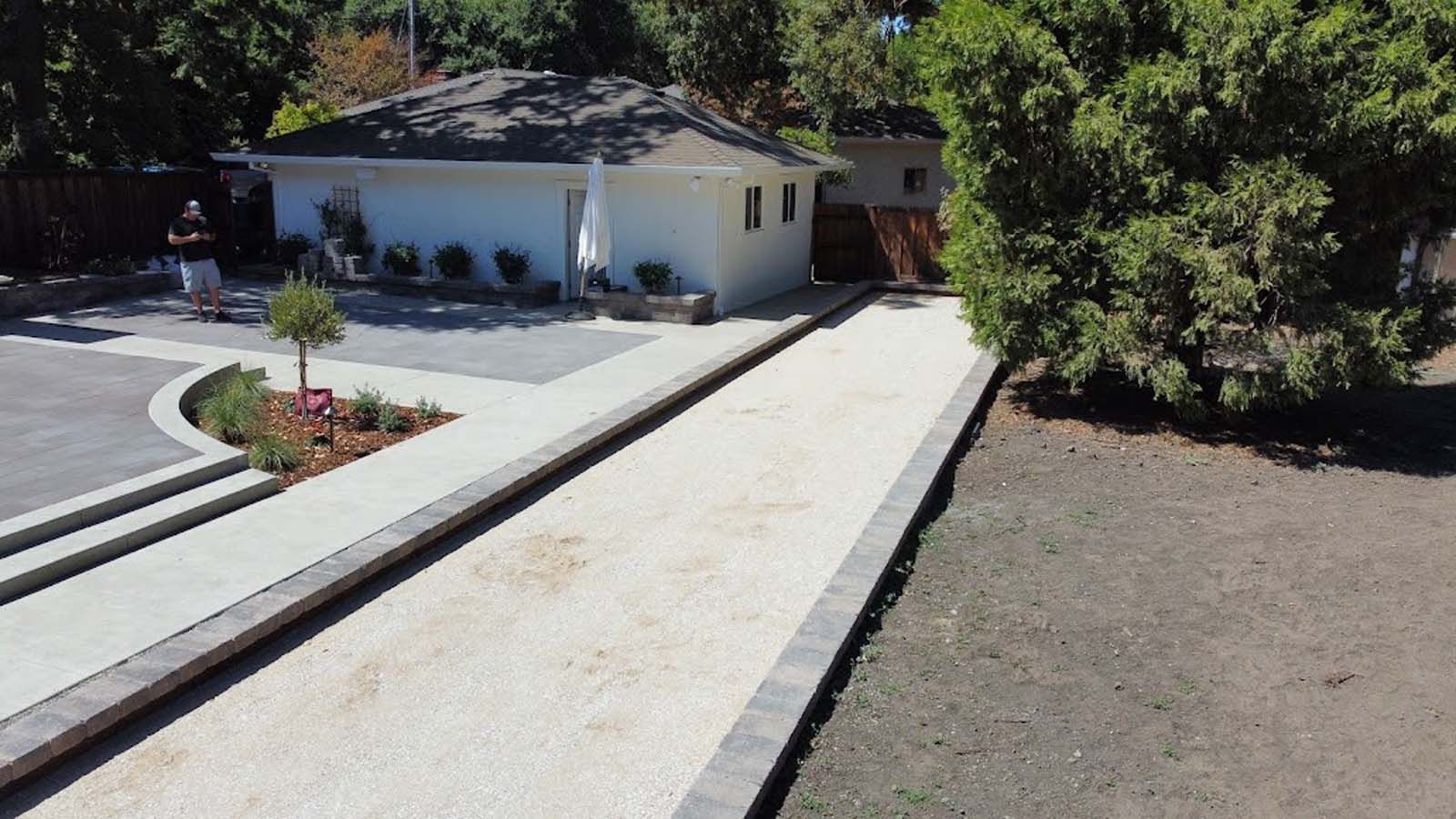 Bocce ball court with white gravel, concrete borders, and a small building in the background.