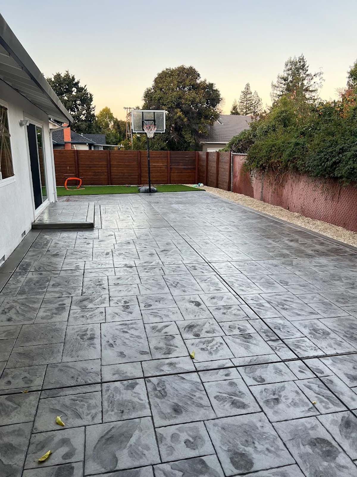 Backyard patio with stamped concrete, basketball hoop, and wooden fence.