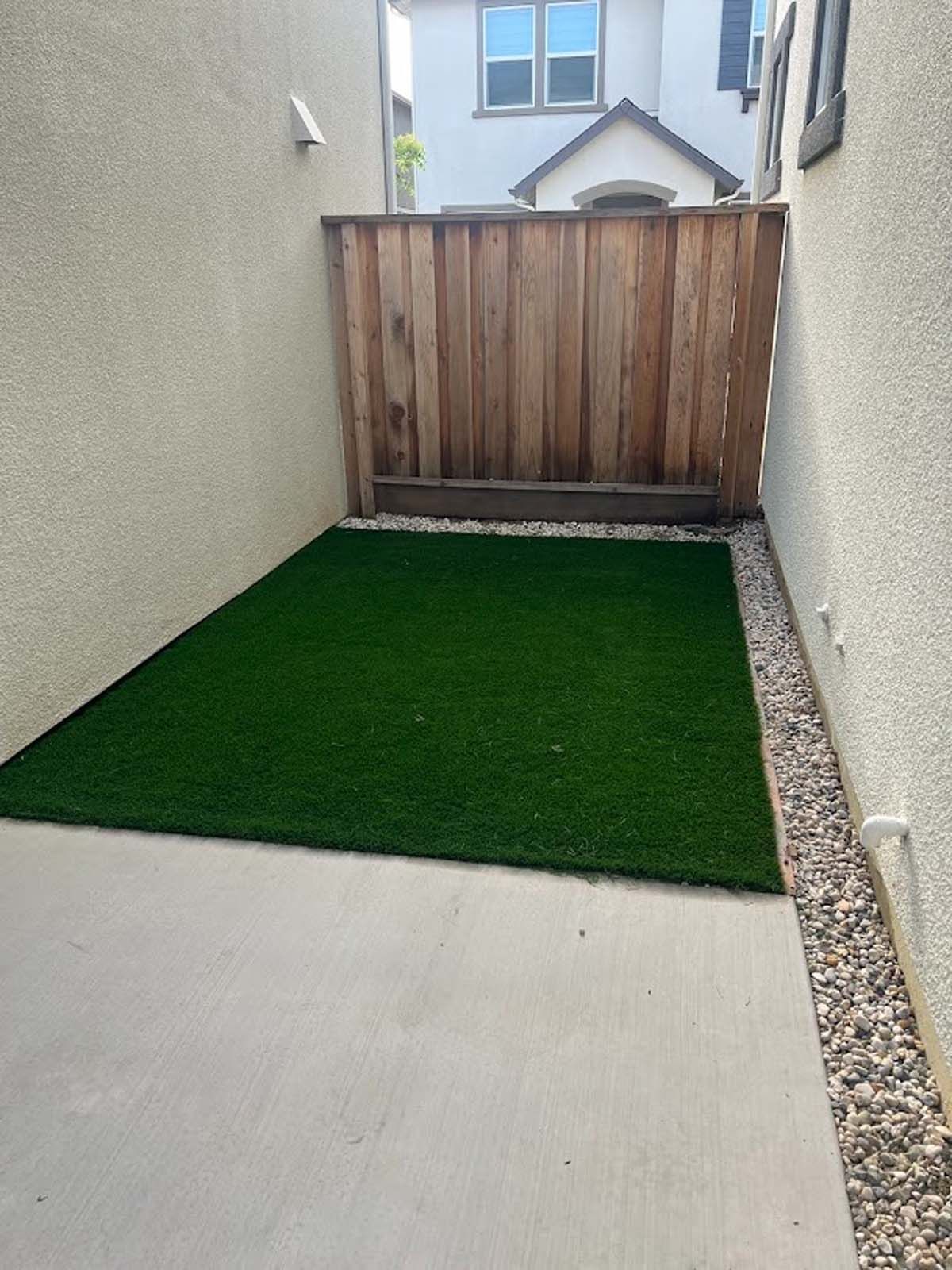 Small backyard with artificial turf, concrete, gravel, and wooden fence.