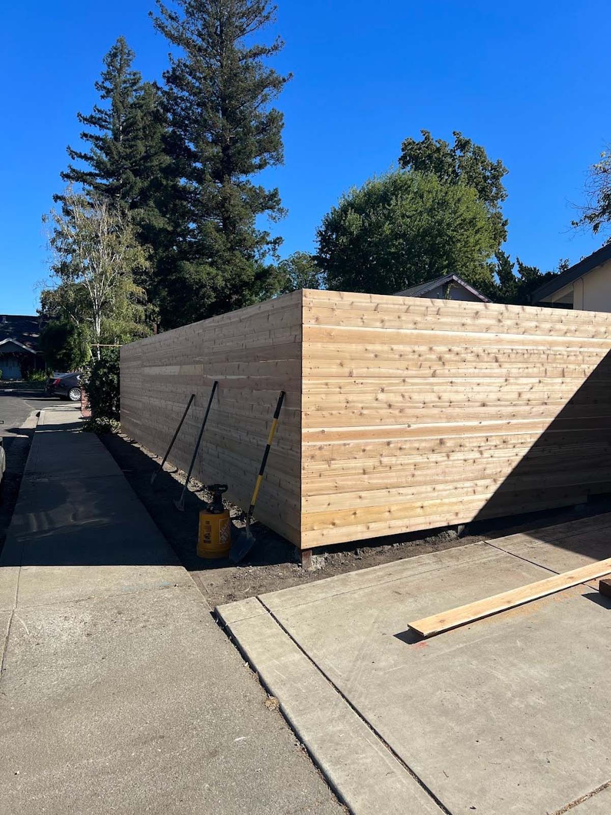 New cedar fence along a sidewalk, with tools visible near the base.