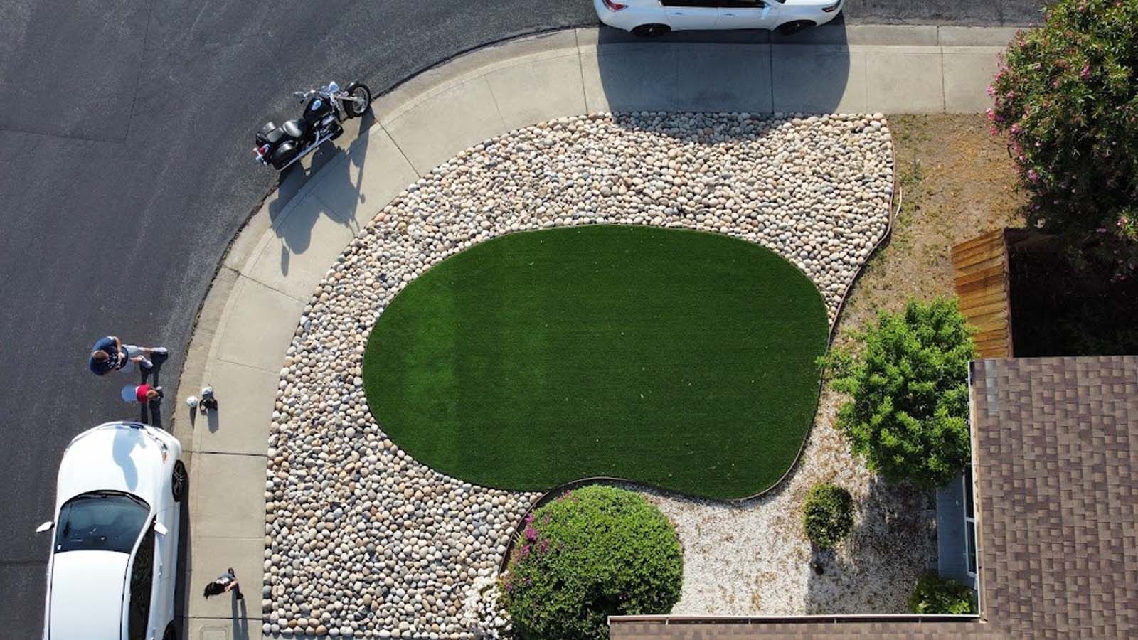 Overhead shot of driveway with a motorcycle, car, and circular lawn surrounded by rocks.