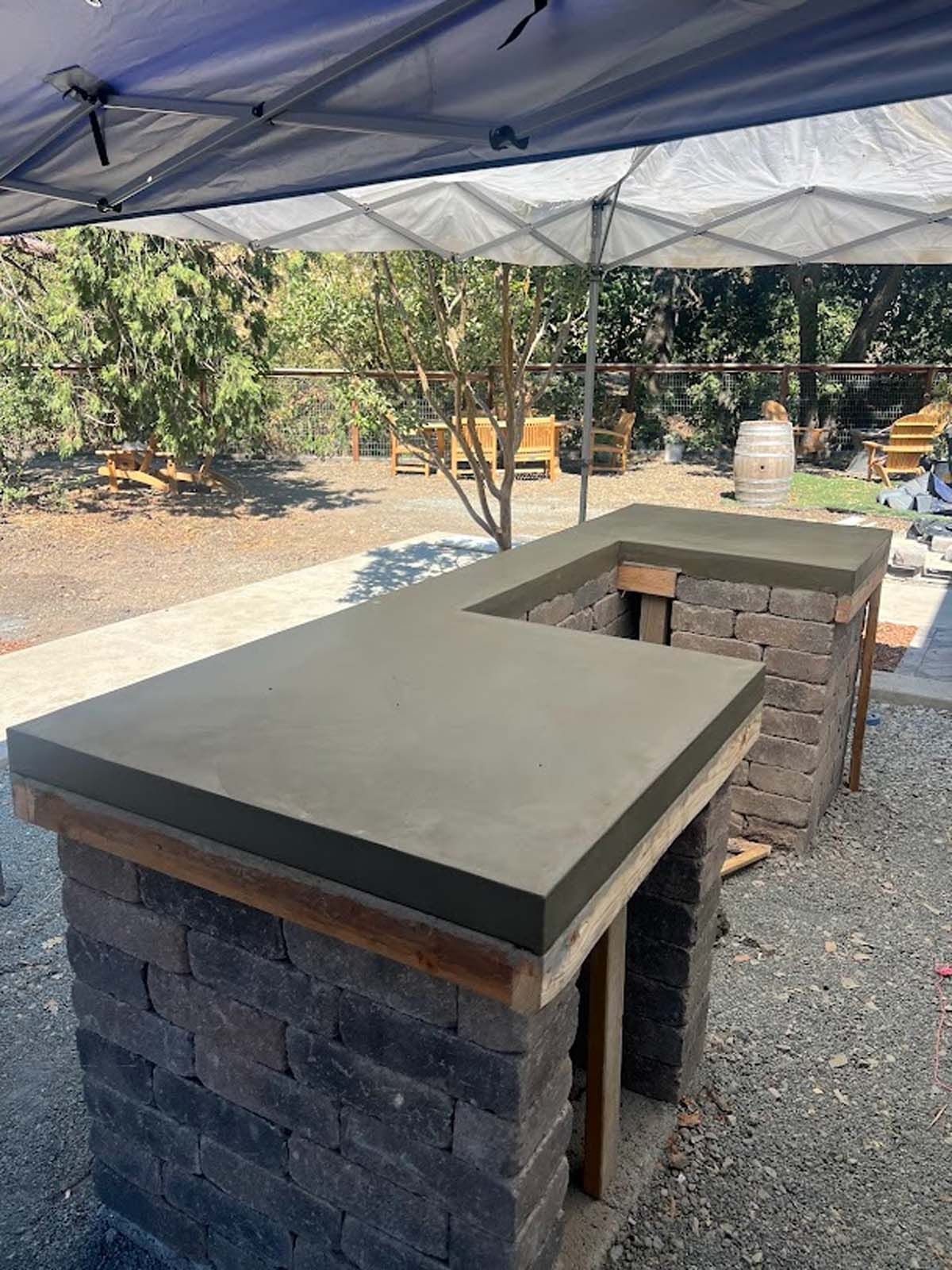 Outdoor bar with gray concrete countertop and brick base, under a white tent.