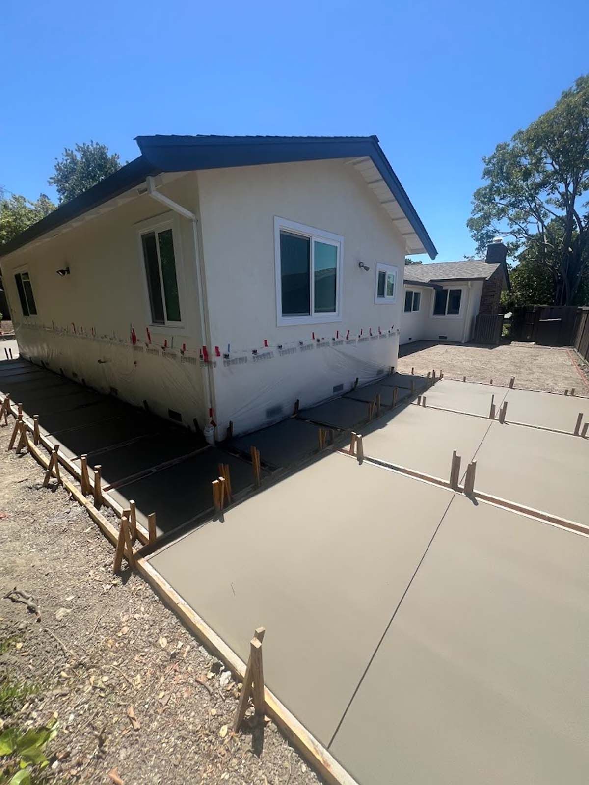 New concrete driveway and walkway next to a light-colored house under construction.