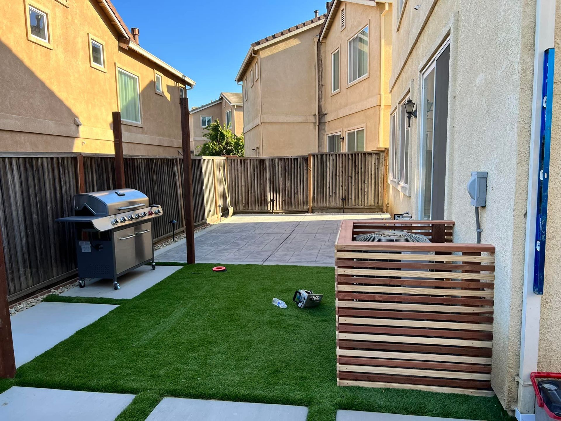 Backyard with grill, artificial turf, and wooden privacy screens. Houses in background.