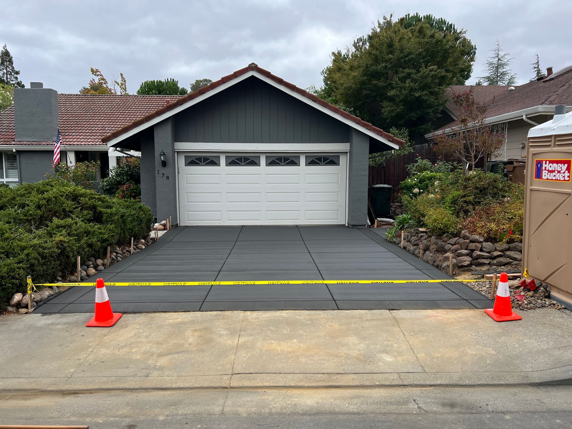 Freshly poured concrete walkway between two houses, bordered by wooden forms and safety cones.