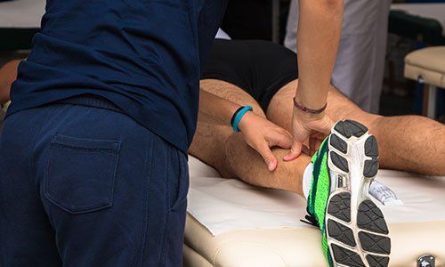 un fisioterapista che massaggia la caviglia di un ragazzo sdraiato a pancia in giu’