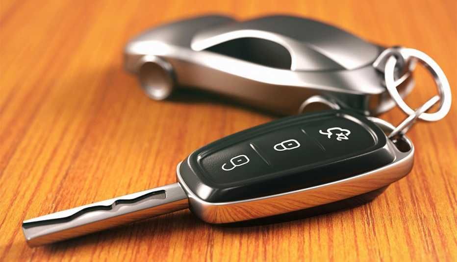 Car keys with key fob on wooden table, car-shaped keychain in background.