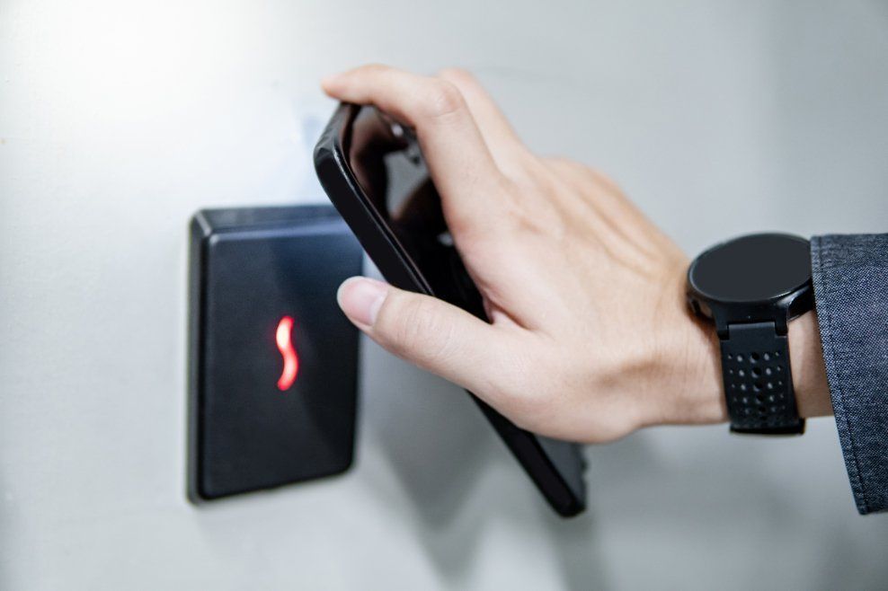 Hand with phone unlocking a security access panel; wrist watch visible.