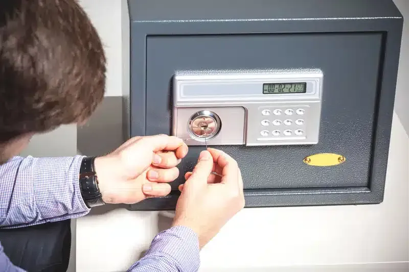 Person using a key to unlock a safe with a digital keypad.