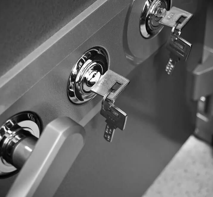Keys inserted in two lock cylinders on a safe door with a handle.