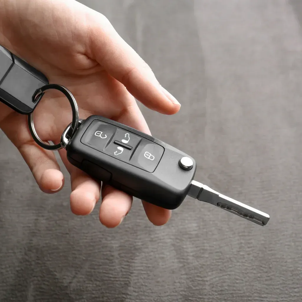 Hand holding a black car key with remote control buttons and metal key blade.