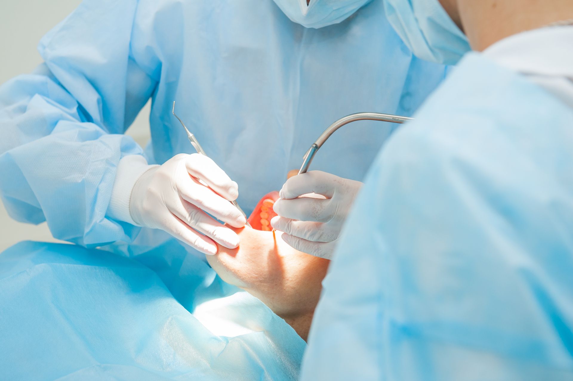 Oral surgeon performing a procedure with dental instruments in a sterile operating setting.