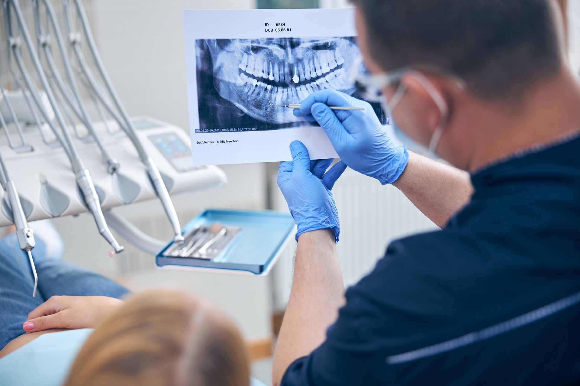 Dental professional reviewing a panoramic X-ray with a patient in a treatment room.
