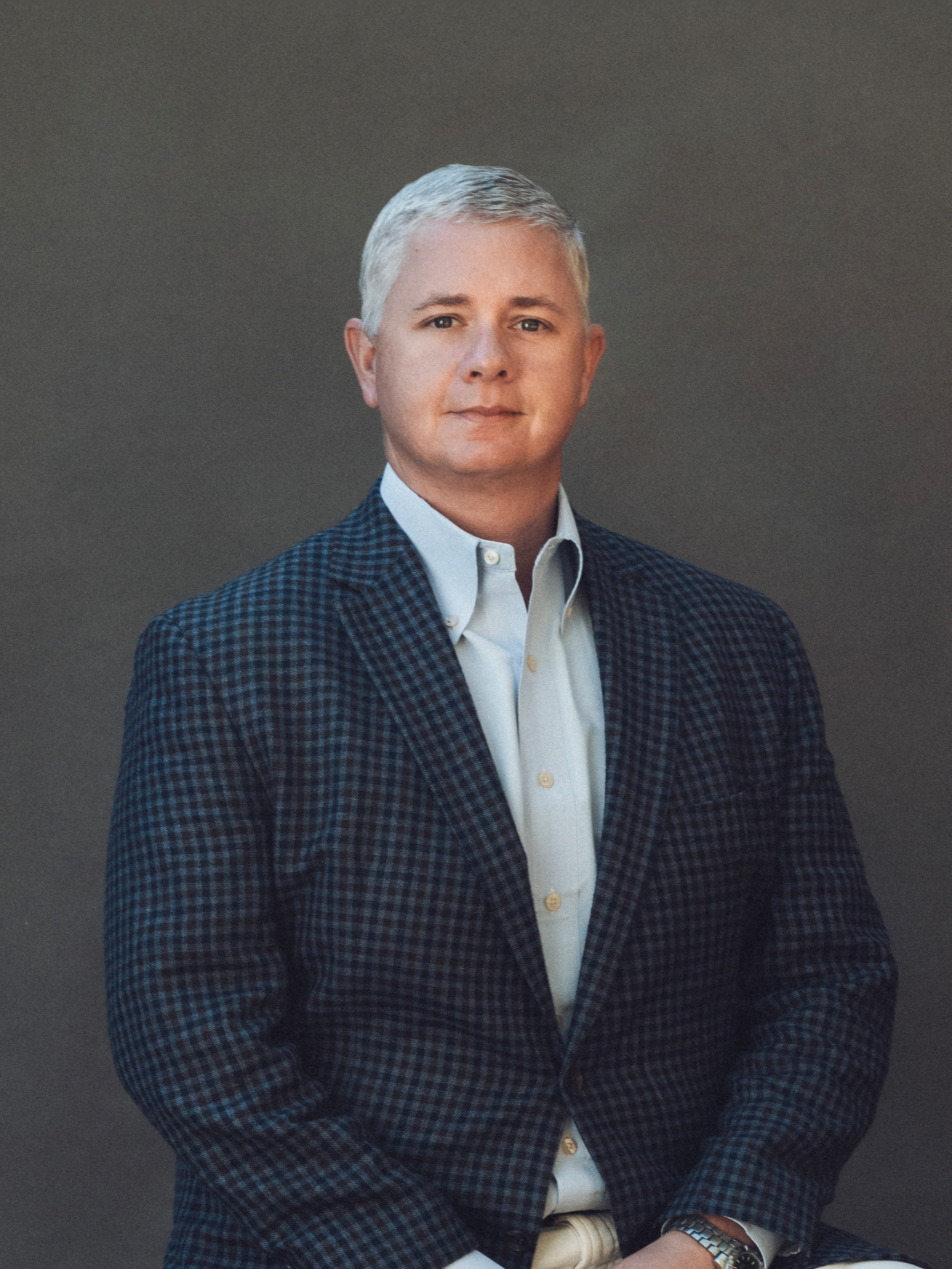 Jack Daniels in a suit and blue shirt is standing in front of a wooden wall.