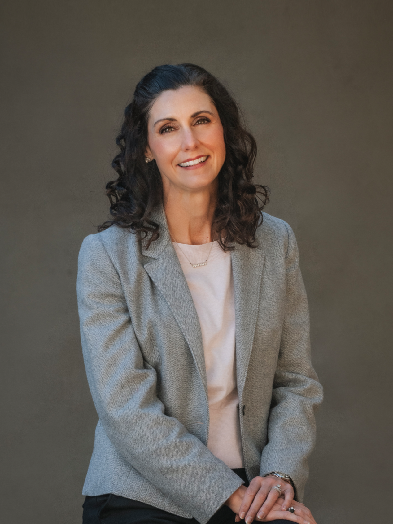 Joslyn Daniels with long brown hair is smiling for the camera in front of a tree.