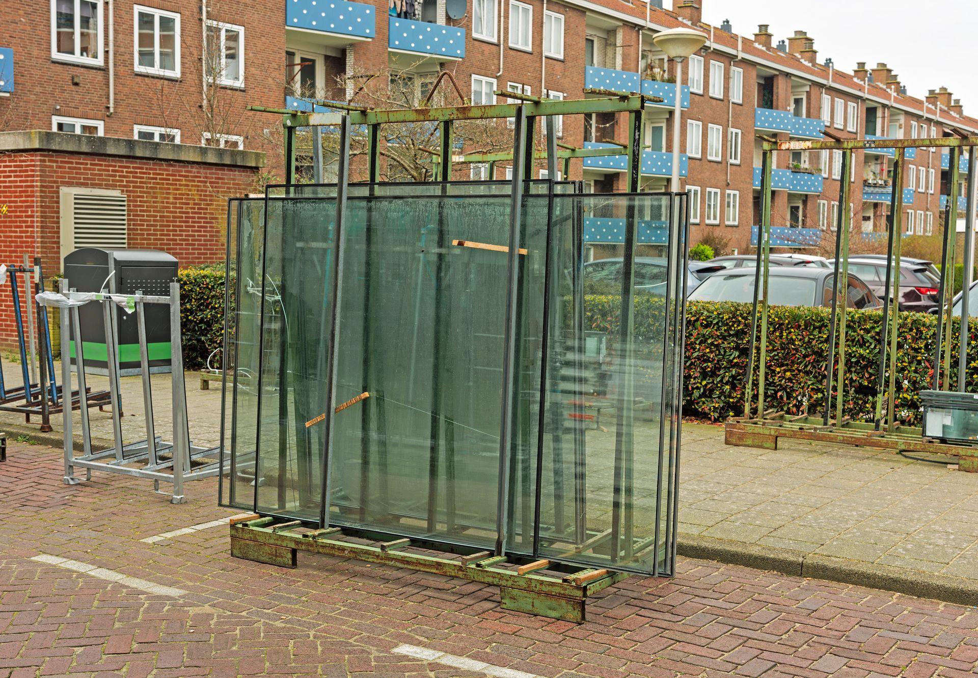 Large glass panels stacked on a pallet on a sidewalk, near a building.