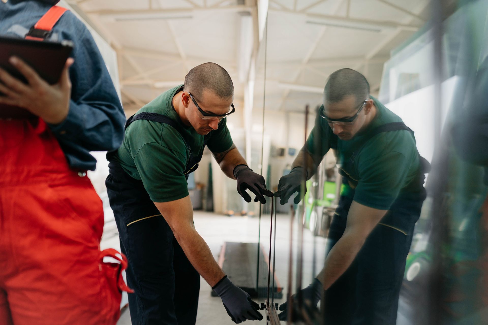 A professional glass cutter, wearing a protective uniform, is moving a glass panel.