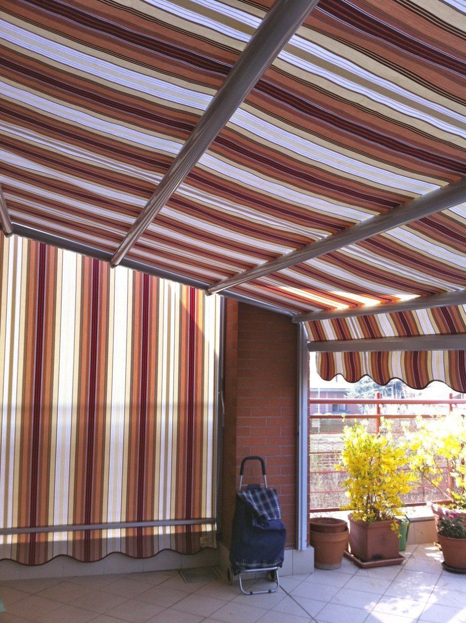 Tenda da interni a strisce sopra un patio con un muro di mattoni e piante in vaso.