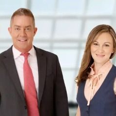 A man in a suit and tie is standing next to a woman in a vest.
