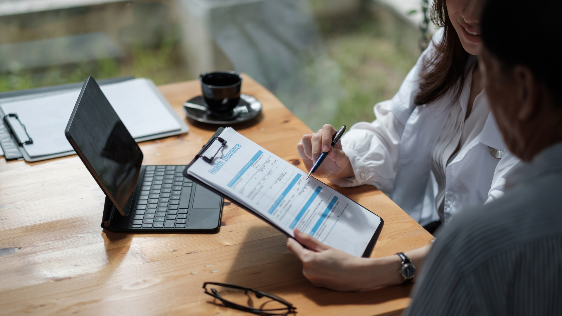 A man and a woman are sitting at a table looking at a clipboard.