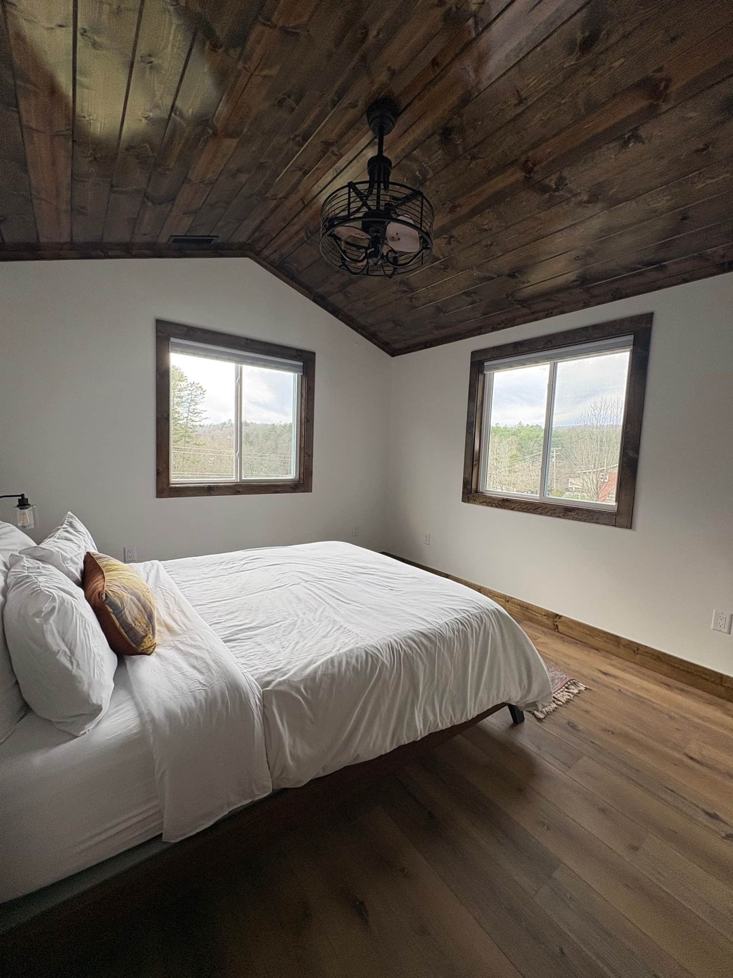 A bedroom with a bed , two windows and a wooden ceiling.