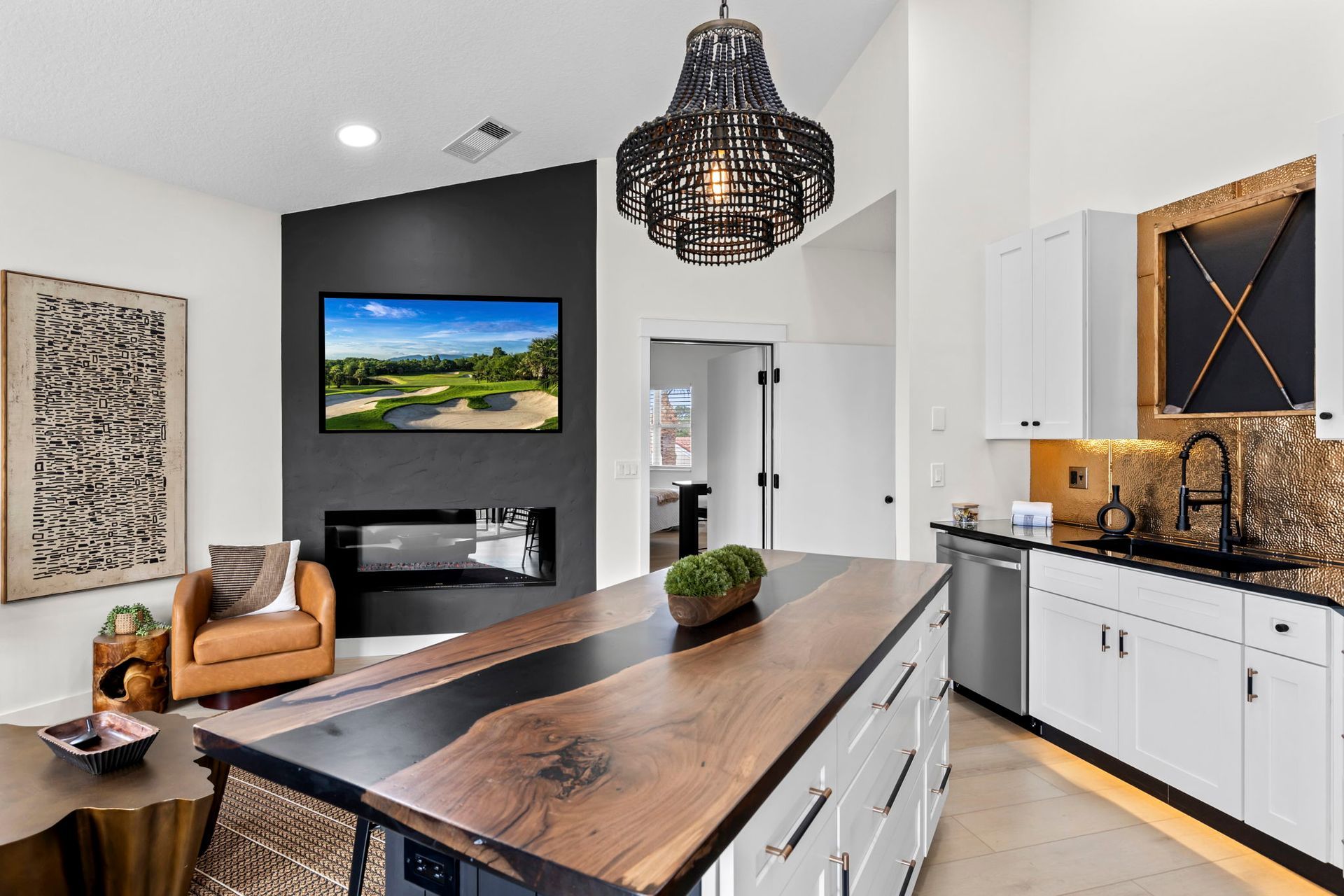 Modern kitchen with island, TV, fireplace, and black chandelier.