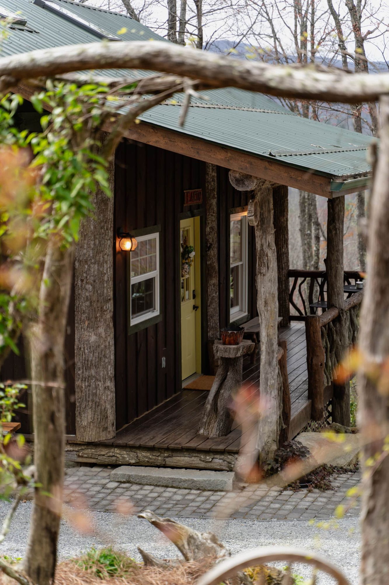 A small cabin with a porch in the woods surrounded by trees.