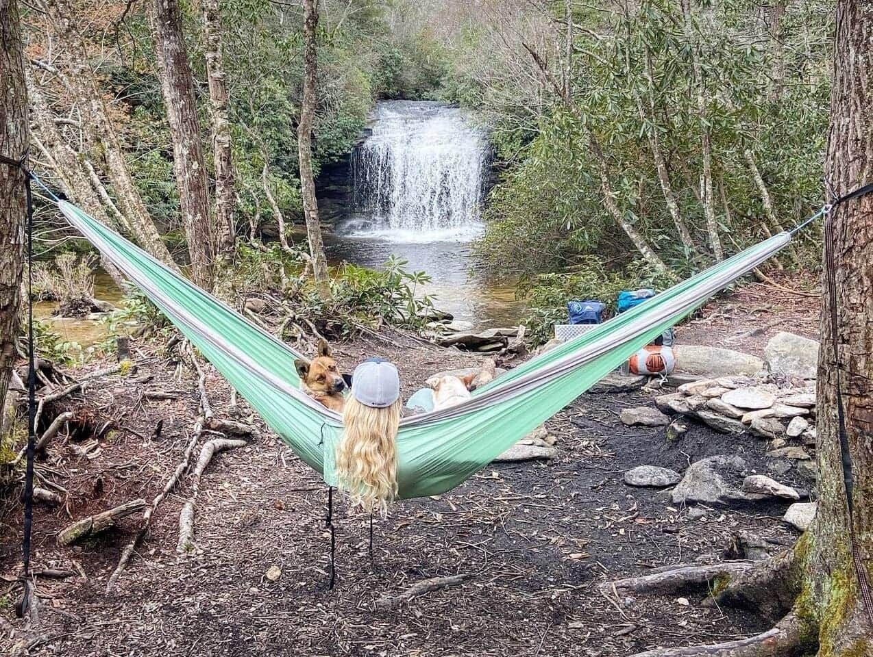 A woman is laying in a hammock in front of a waterfall.