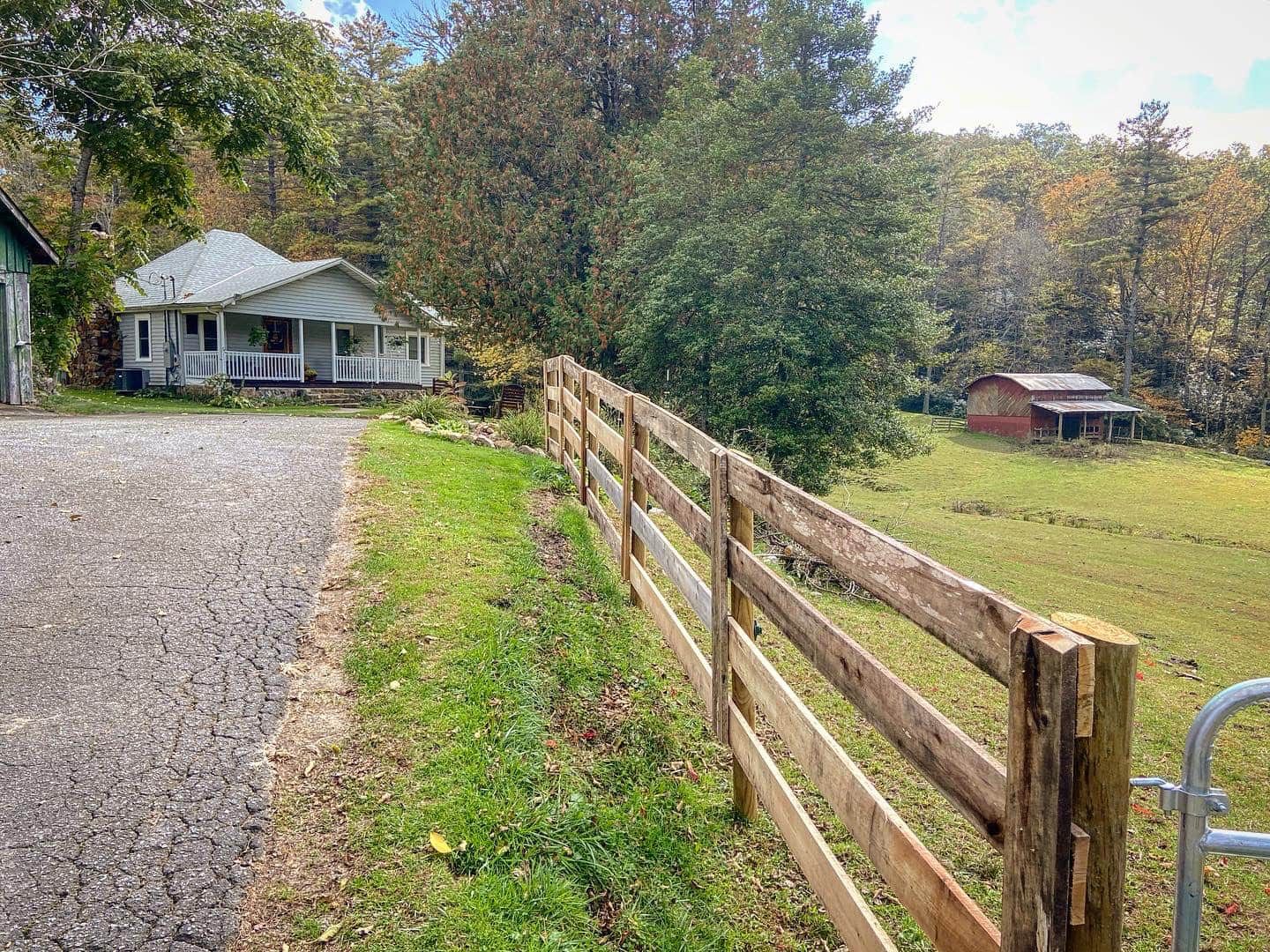 A wooden fence surrounds a grassy field in front of a house.