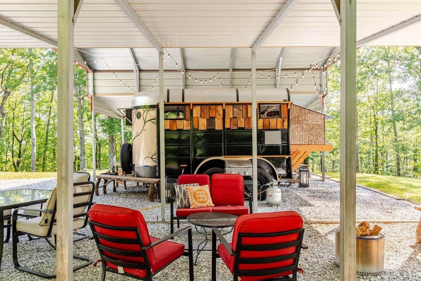 A trailer is parked under a covered patio with chairs and a table.