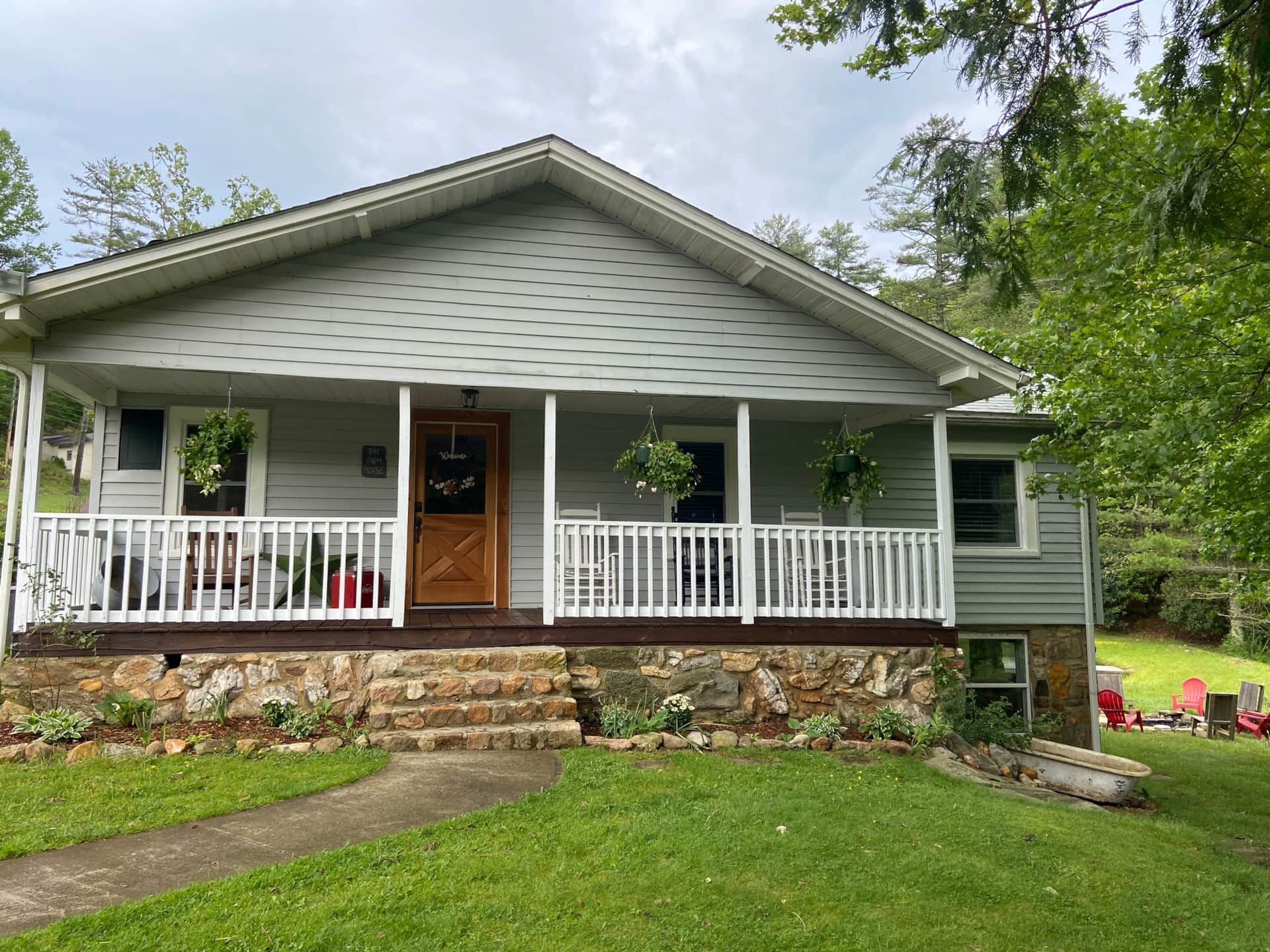 A house with a porch and stairs in the middle of a lush green field.