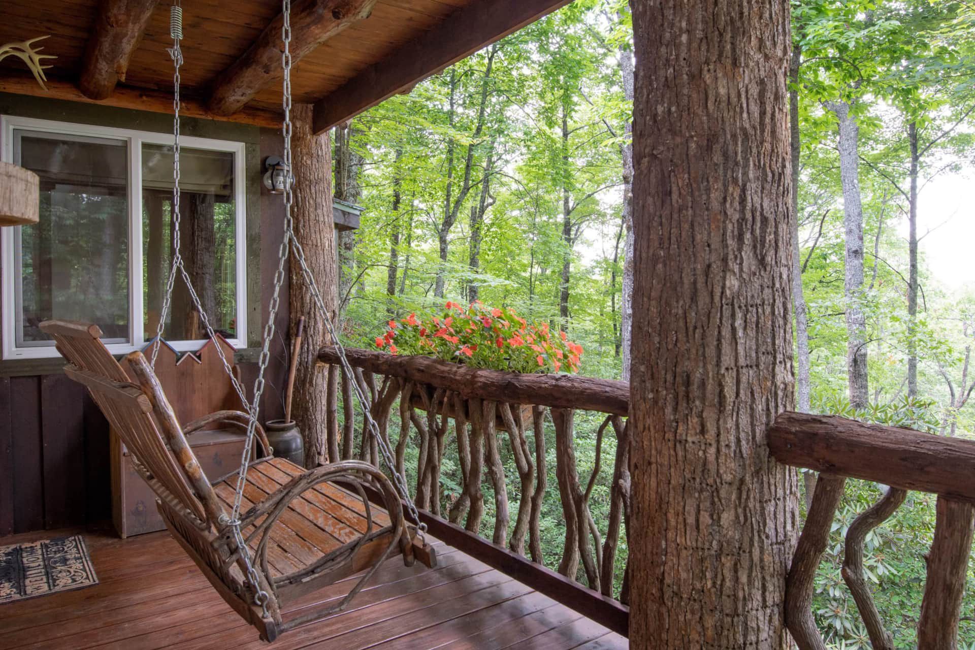 A porch with a wooden swing hanging from a tree.