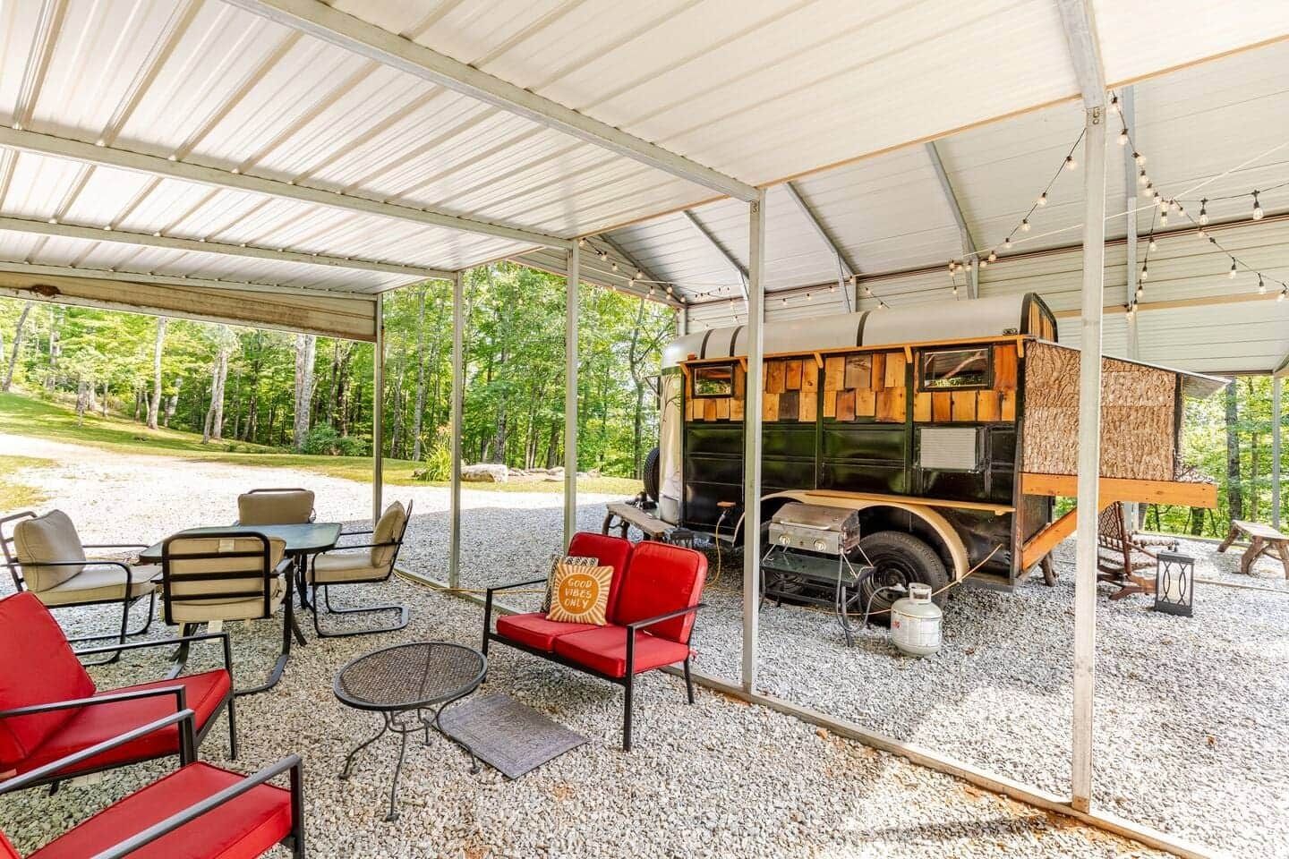 A covered patio area with a couch , chairs , tables and a trailer.
