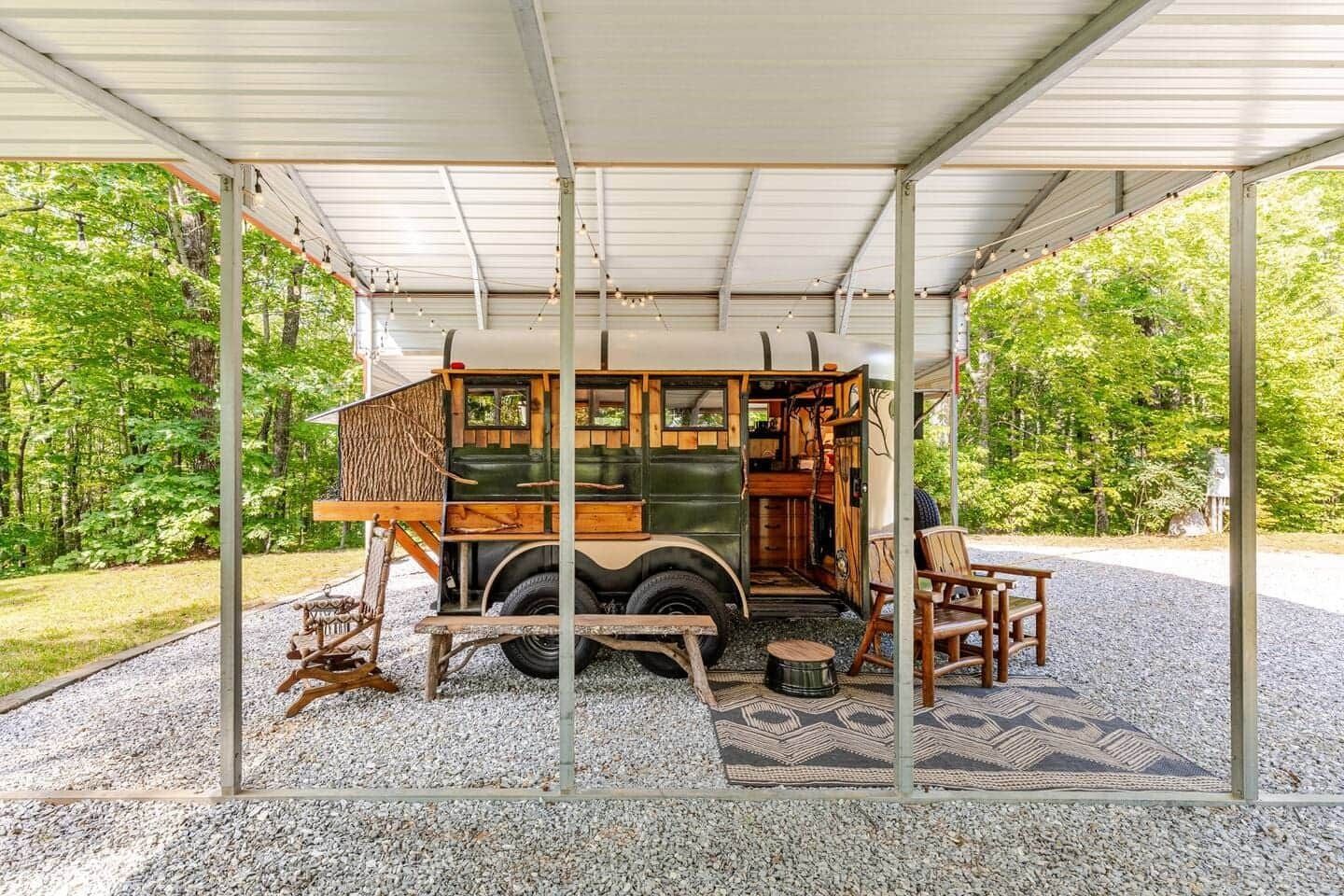 A trailer is parked under a carport with a picnic table and chairs.