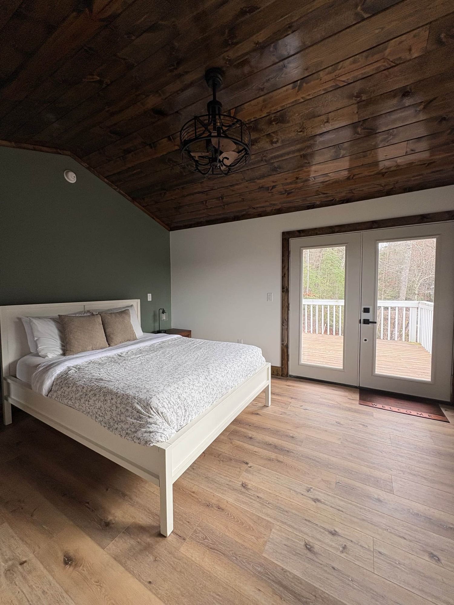 A bedroom with a king size bed , hardwood floors and a wooden ceiling.