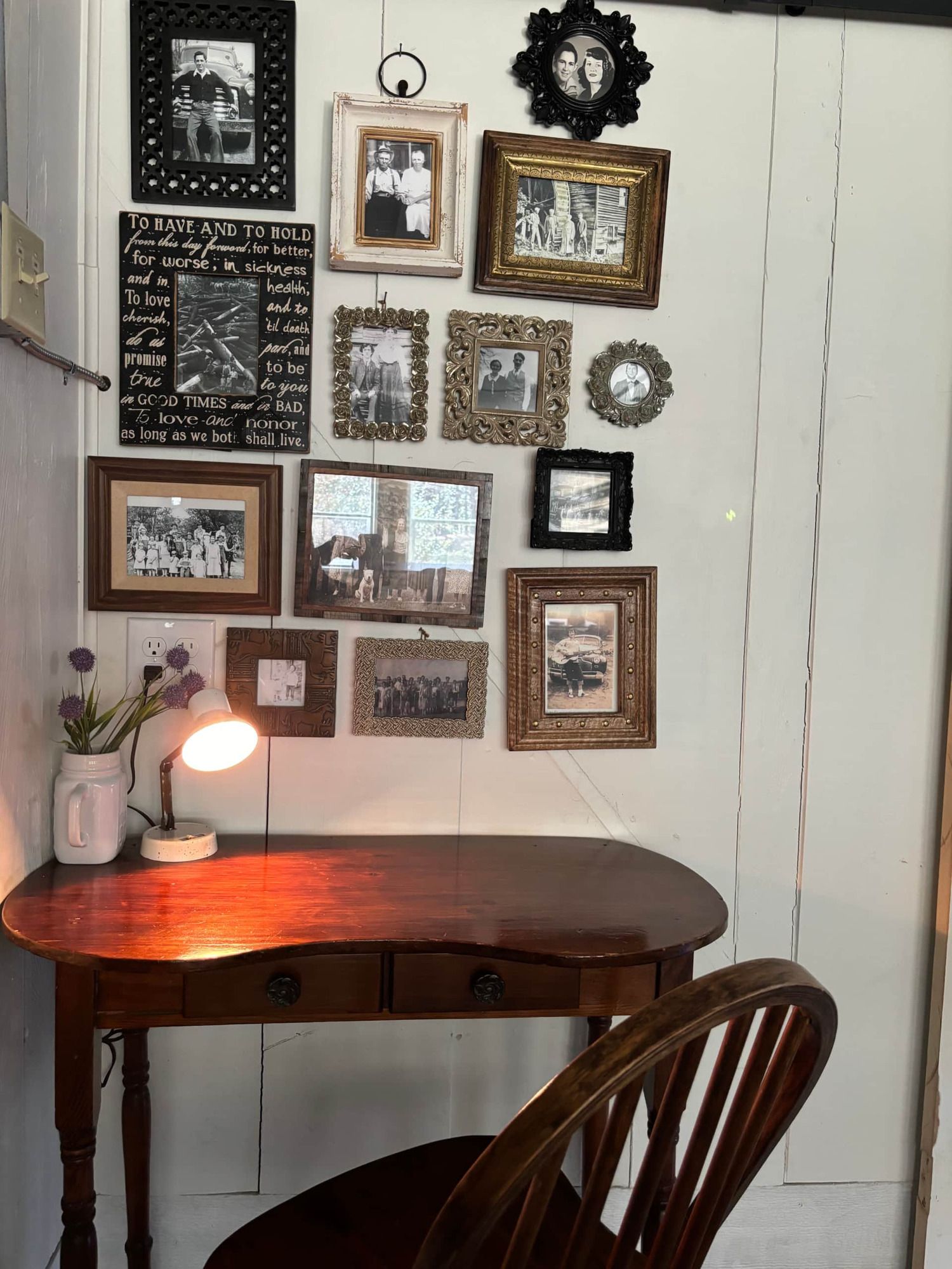 A desk with a lamp and a chair in front of a wall with pictures on it