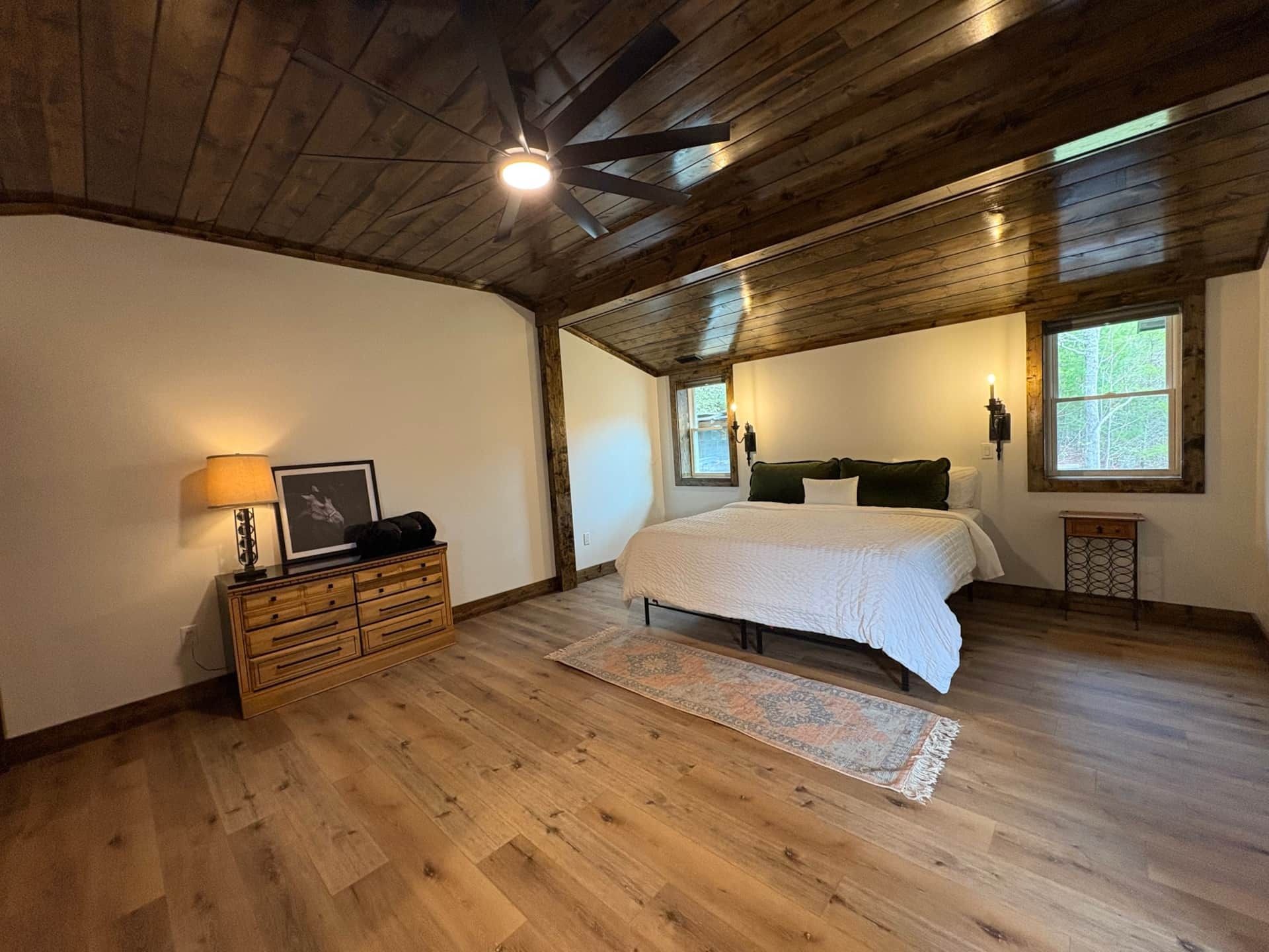 A bedroom with a bed , dresser , lamp and ceiling fan.