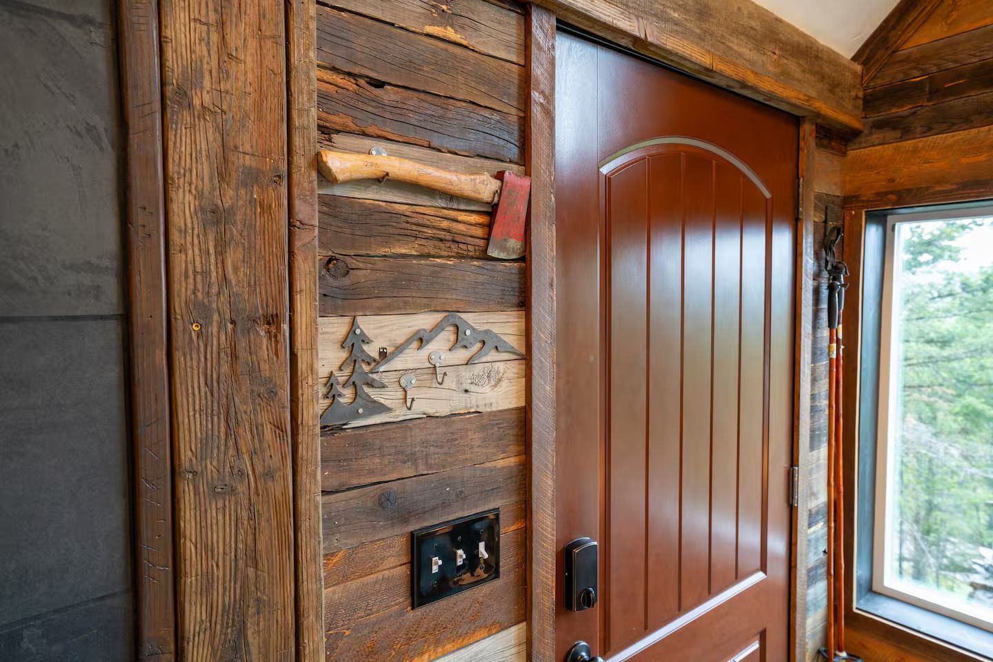 A red door is sitting on a wooden wall next to a window.