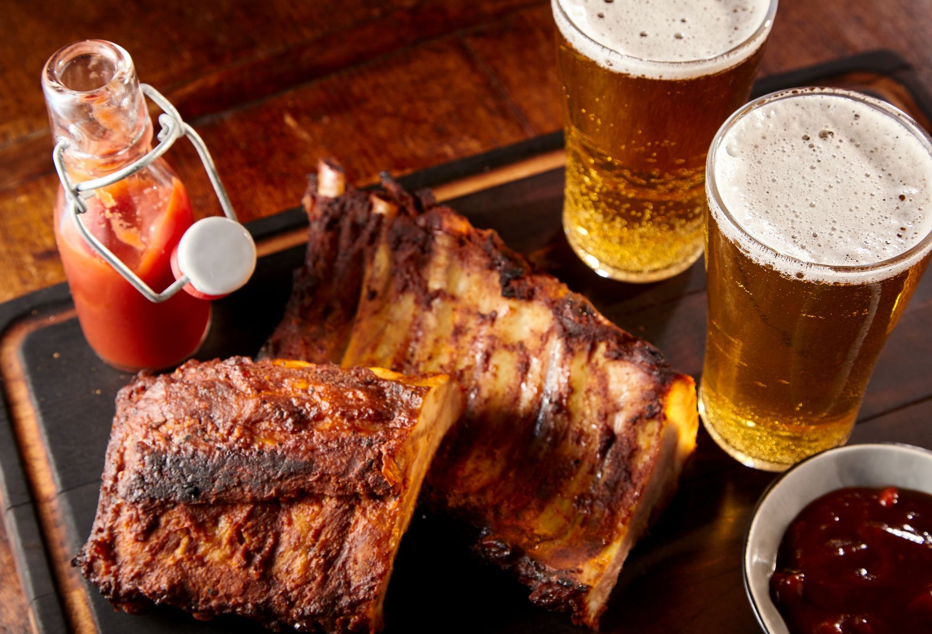 Grilled ribs with beer and sauce on a wooden tray.