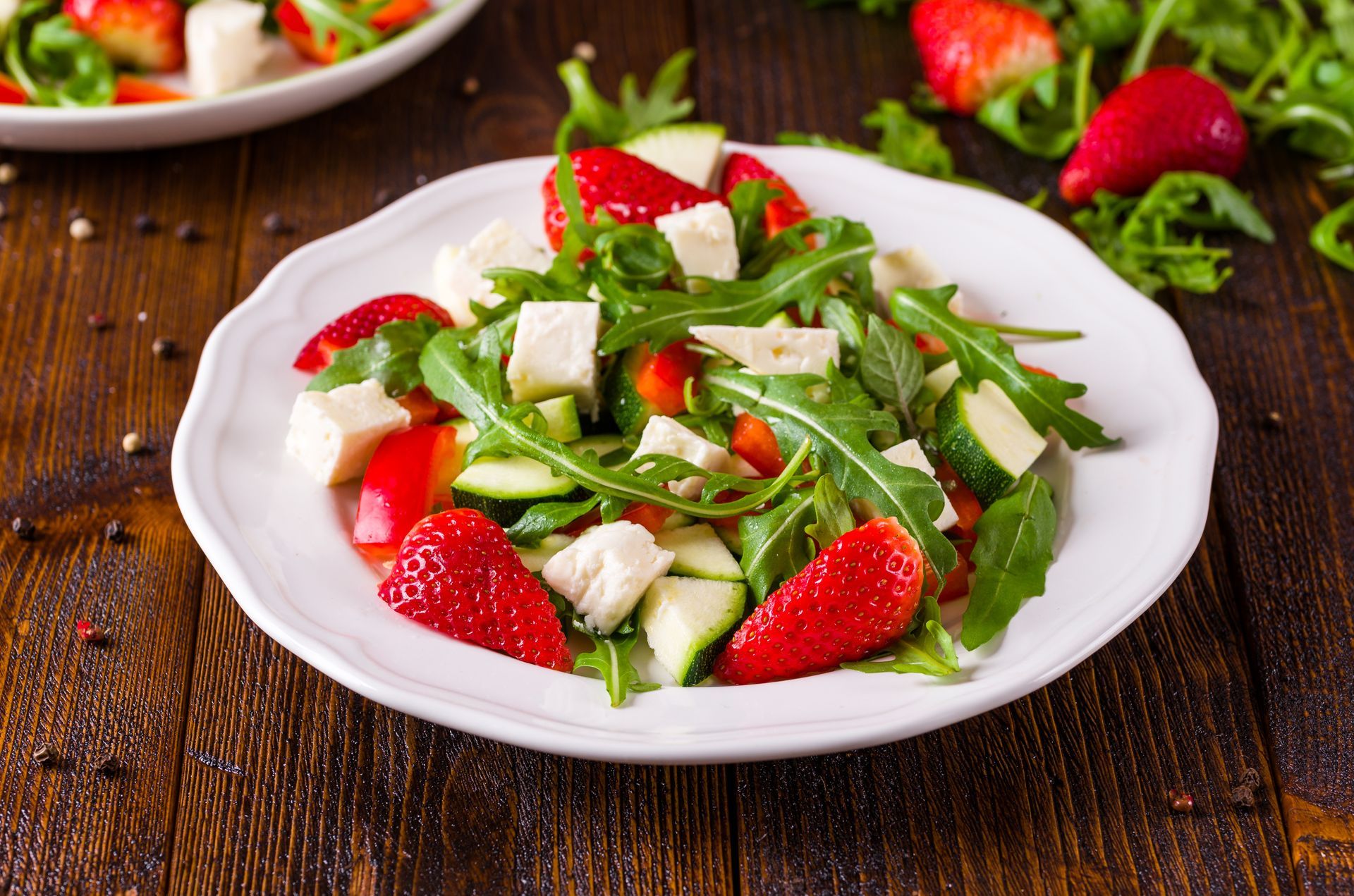 Strawberry, arugula, feta salad on white plate; wooden table.