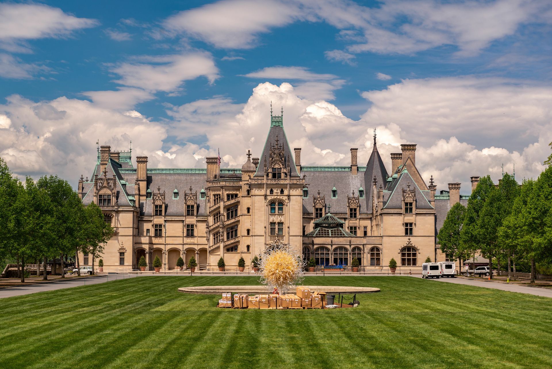 Biltmore Estate, Asheville, North Carolina, on a sunny day. Green lawn, ornate stone building, blue sky, and puffy clouds.