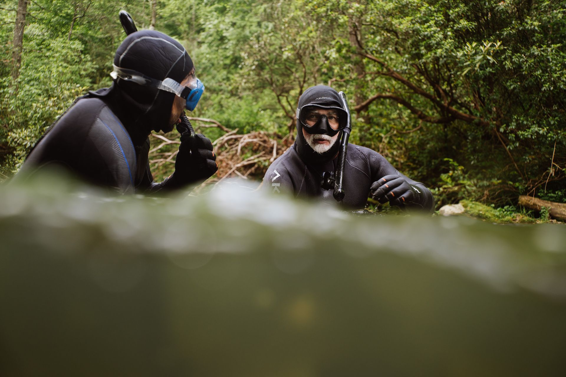 Diver in black wetsuit with scuba gear, surfacing in gray water.