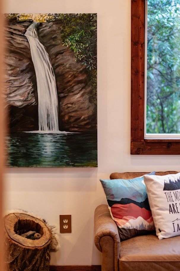 Two people in a rustic living room: one in a hammock, the other on a couch. Nature paintings and decor surround them.