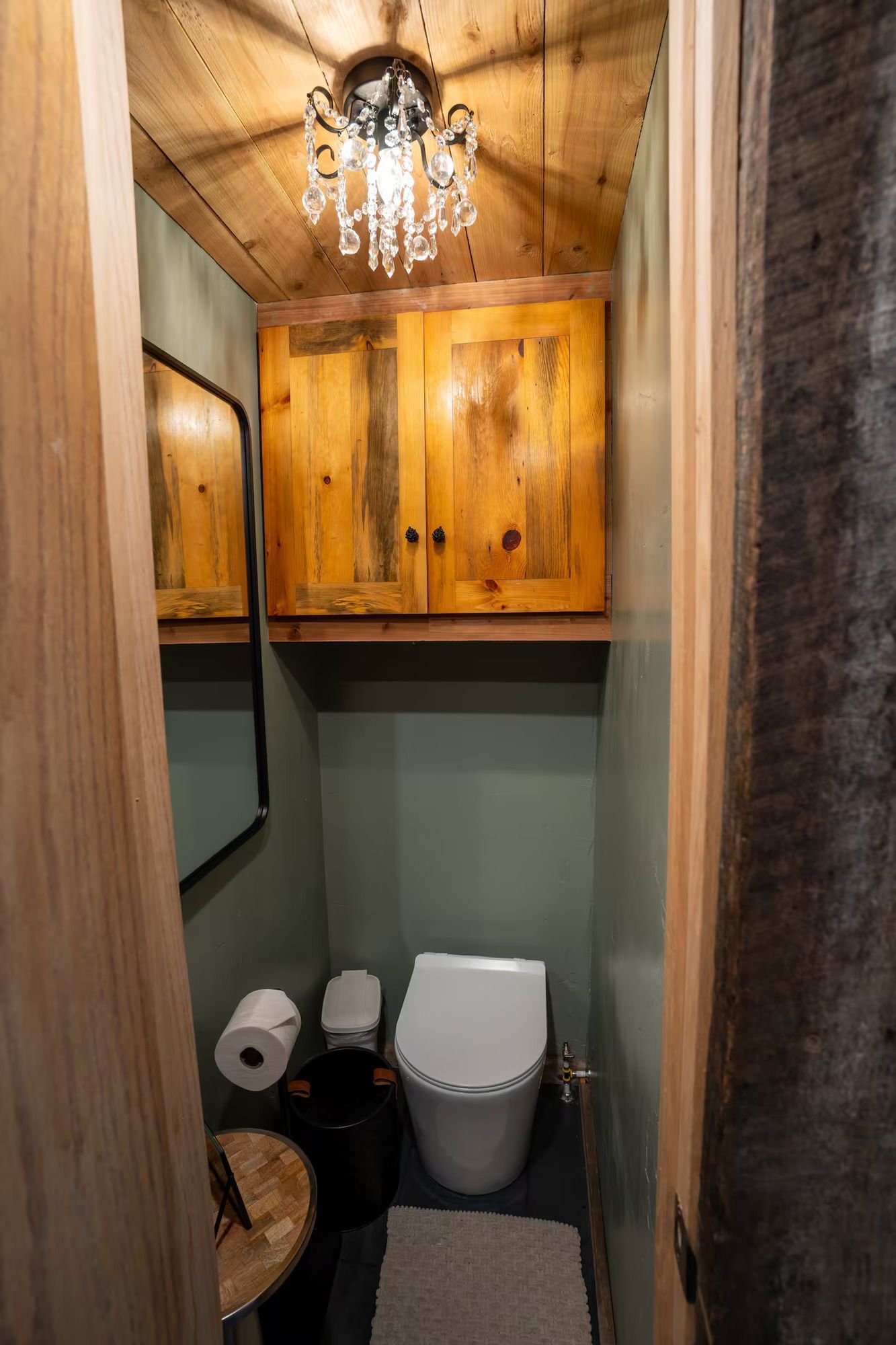 A small bathroom with a toilet , sink , mirror and chandelier.