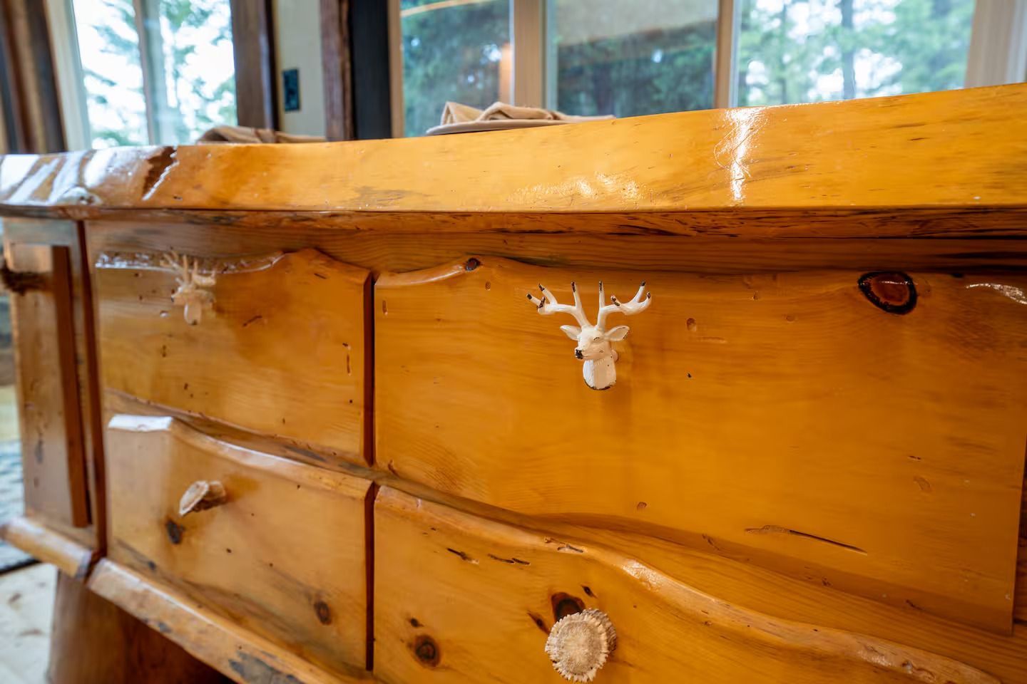 A close up of a wooden dresser with a deer head on the drawer.