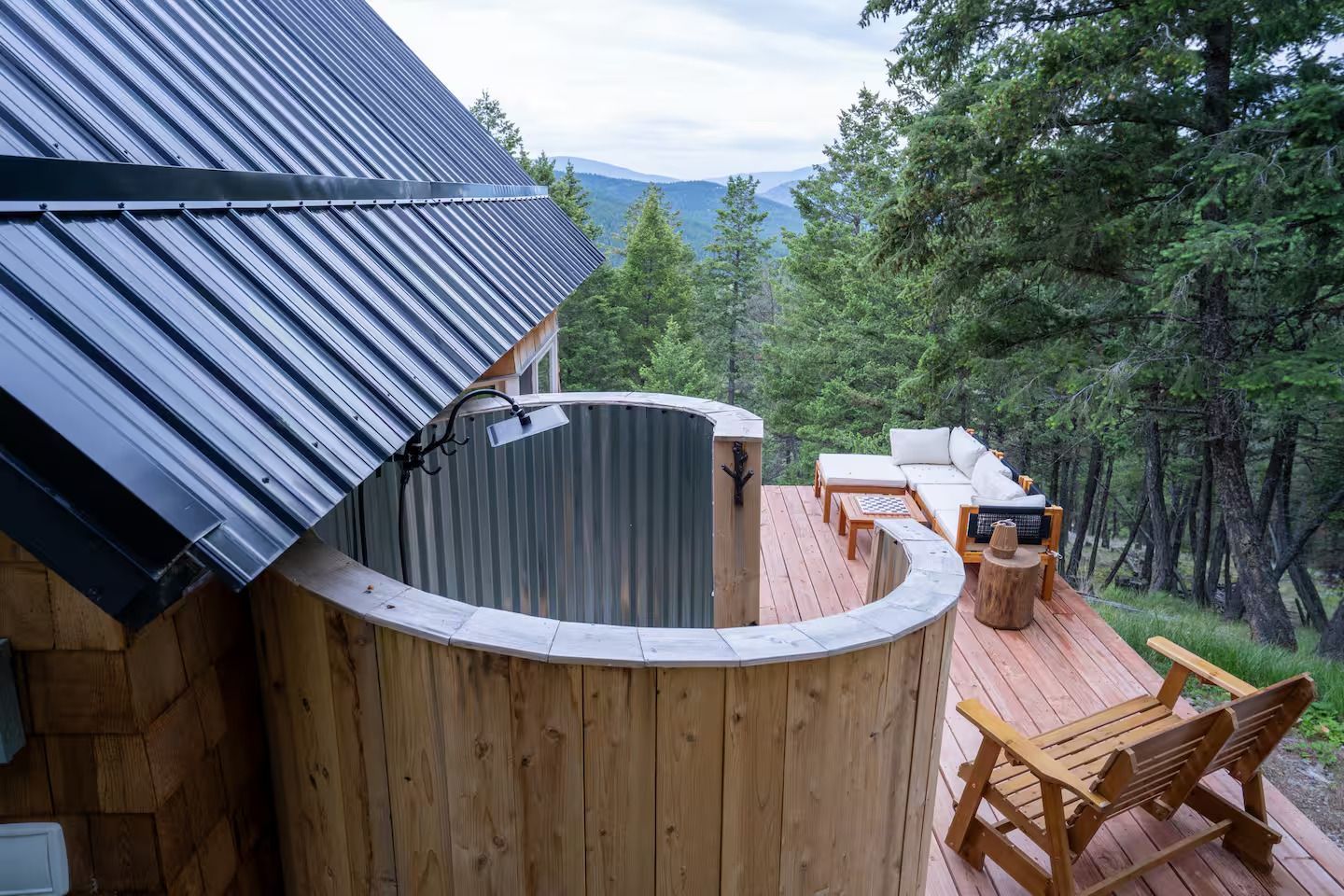 A wooden deck with a circular shower on the side of a house surrounded by trees.
