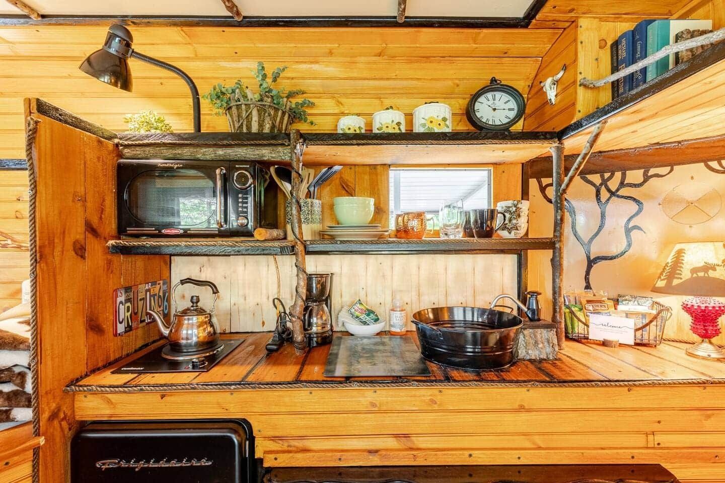 A wooden kitchen with a stove , microwave , and shelves.