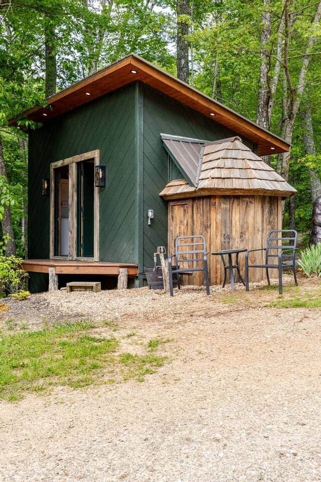 A small green house with a wooden roof is sitting in the middle of a forest.